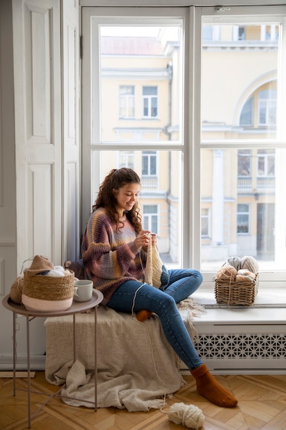 Free photo full shot smiley woman knitting at home