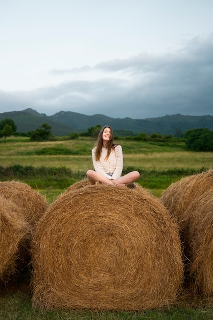 Free photo full shot smiley woman sitting on haystack