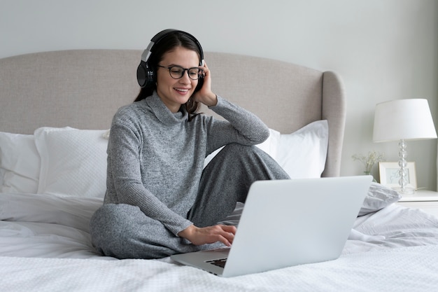 Full shot smiley woman with laptop in bedroom