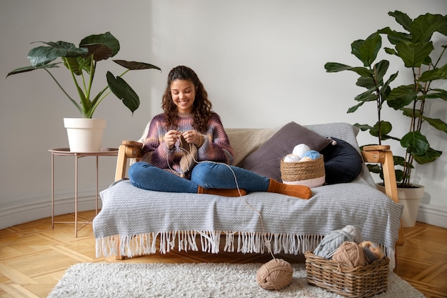 Free photo full shot smiley young woman knitting on couch