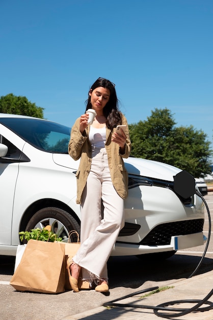 Full shot woman drinking coffee by the car