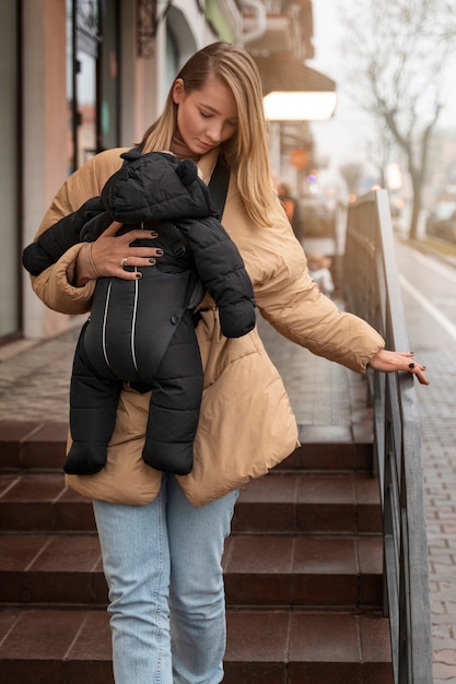 Free Photo full shot woman holding baby in carrier