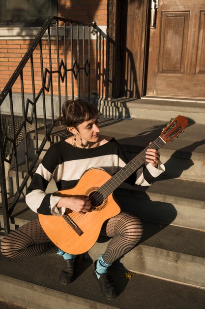 Full shot woman playing the guitar outdoors