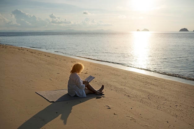 Free Photo full shot woman reading on beach