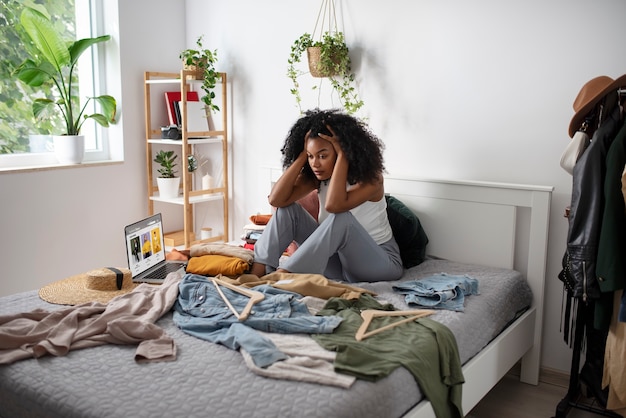 Full shot woman sitting in bed with clothes