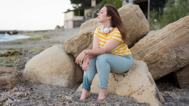 Free Photo full shot woman sitting on rocks at beach