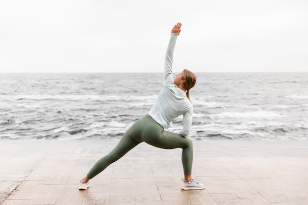 Full shot woman stretching at seaside