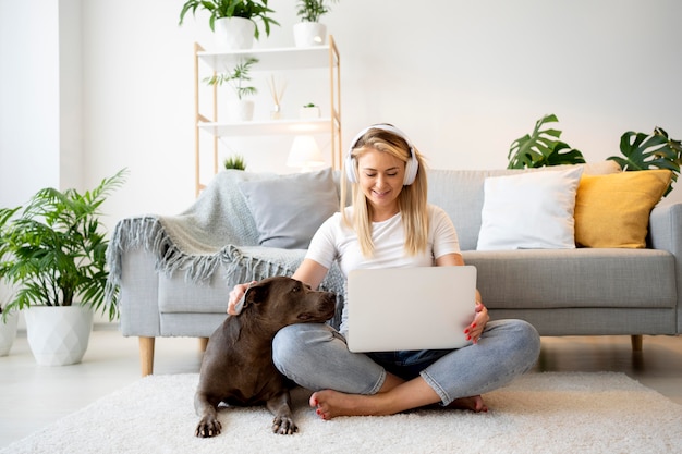 Full shot woman with laptop and dog on floor