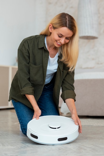 Full shot woman with robotic vacuum cleaner at home