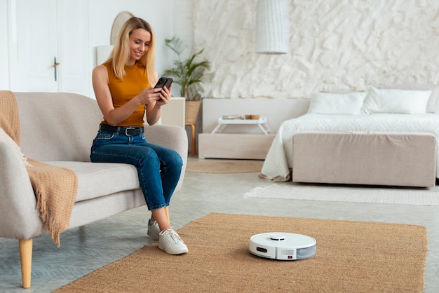 Full shot woman with robotic vacuum cleaner at home