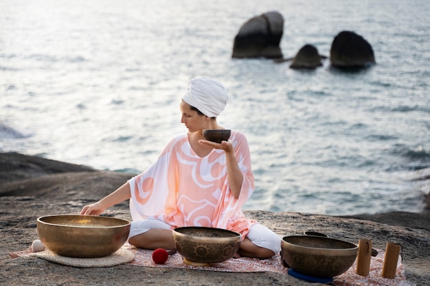 Free Photo full shot woman with singing bowls on beach