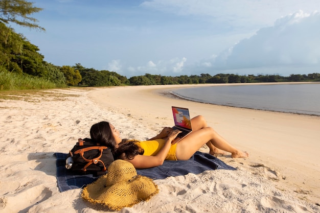 Free photo full shot woman working at beach with laptop