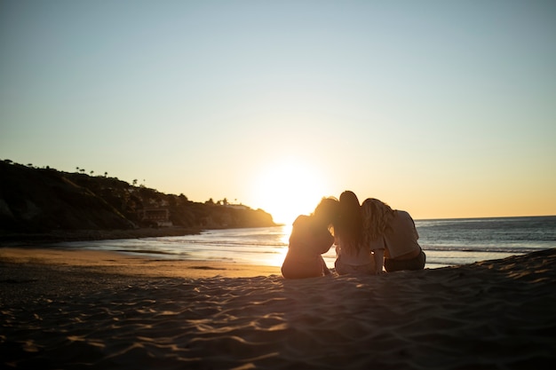 Free photo full shot women sitting on beach at sunset