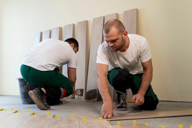 Full shot workers tiling floor indoors