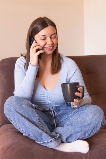 Full view of smiling woman sitting at home talk on phone