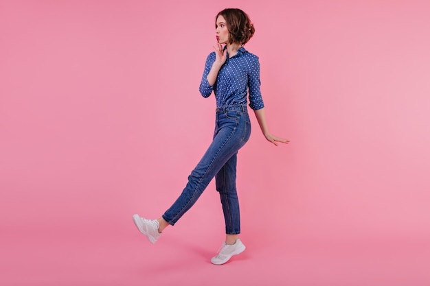 Fulllength photo of shapely glad girl in white sneakers Slim debonair young woman in jeans posing on pastel background