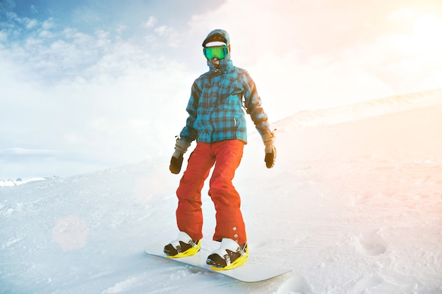 Free photo fully equipped and covered from cold beginner snowboarder wears snow goggles, posing on the top of the mountain