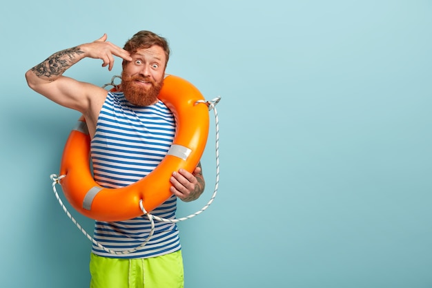 Free photo funny boarswain keeps finger near temple, pretends shooting himself, wears striped vest