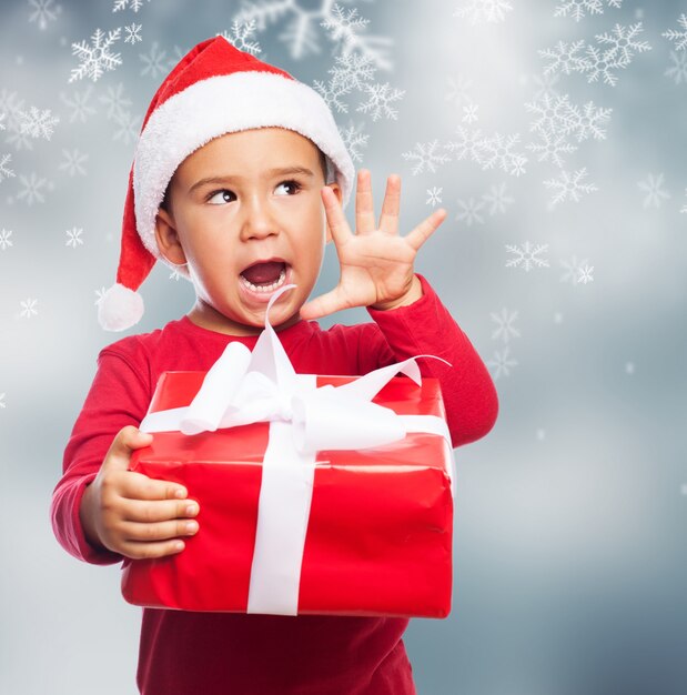 Funny child holding a christmas gift with his right hand