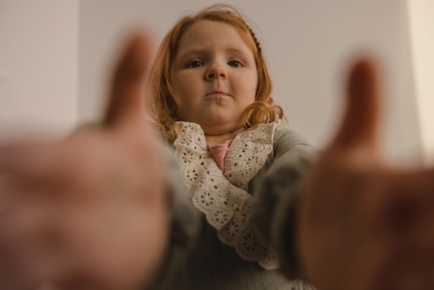 Free photo funny chubby caucasian little girl with red hair reaches for camera taking selfie on white background children concept