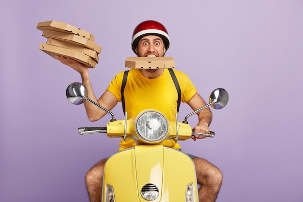 Free Photo funny deliveryman driving yellow scooter while holding pizza boxes