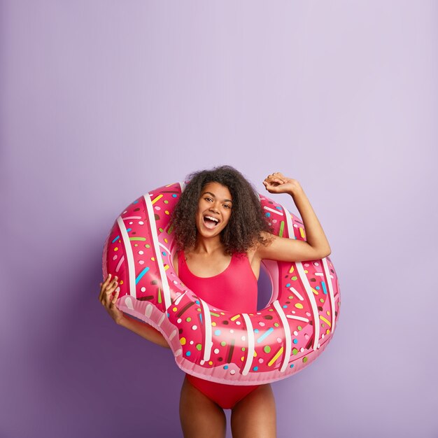 Funny energetic young woman with curly hair posing with pool floaty