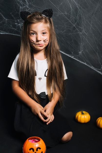 Free photo funny girl in cat costume sitting near jack-o-lantern bucket