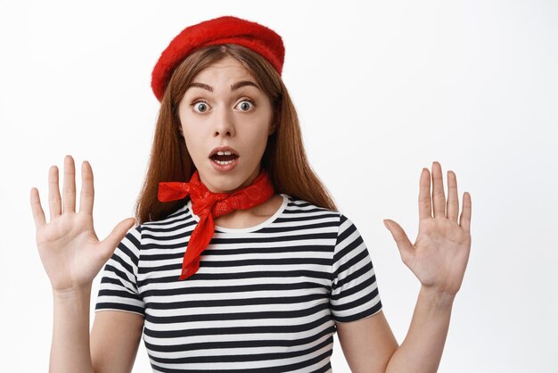 Funny girl mime look surprised as raising hands leaning on invisible wall during pantomime performace wearing red beret and scarf white background