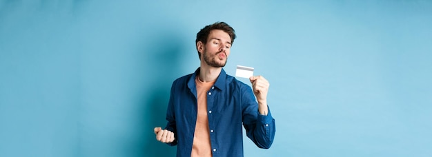 Free Photo funny guy kissing his plastic credit card and looking satisfied shopping with discounts standing on