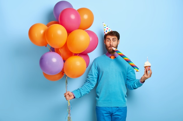 Free photo funny guy with birthday hat and balloons posing in blue sweater