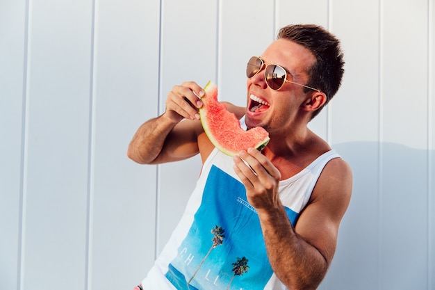 Free photo funny handsome man in sunglasses eating yummy watermelon, laughing loud