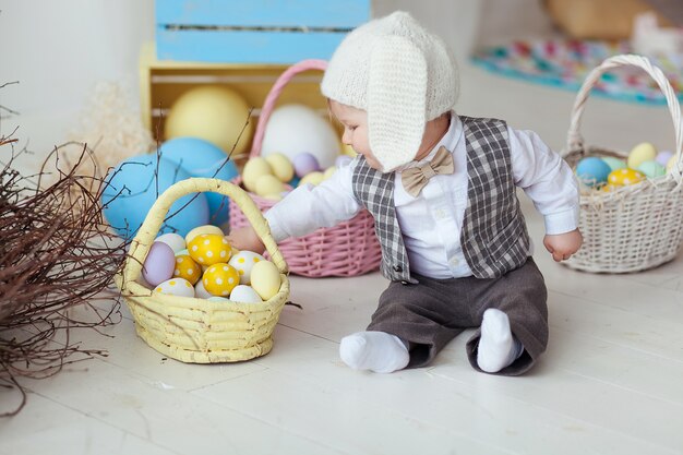 Funny happy baby boy in hat, tie bow and suit playing with Easter eggs. 