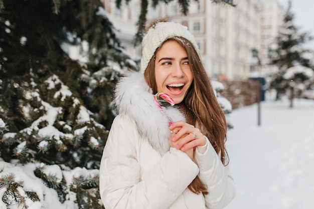 Free photo funny joyful winter woman with lollypop in city. having fun around snow, crazy mood, smiling, positive brightful emotions. new year coming, cold weather, happy time.