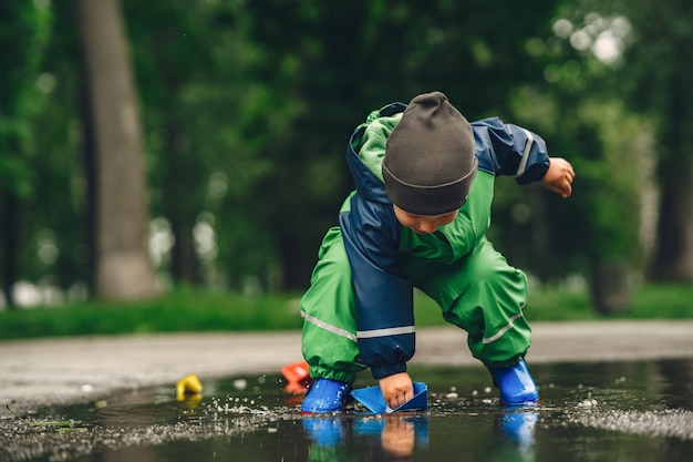 Free photo funny kid in rain boots playing in a rain park