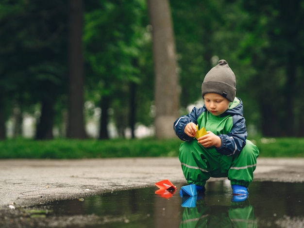 Free Photo funny kid in rain boots playing in a rain park