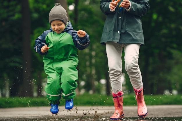 Funny kid in rain boots playing in a rain park