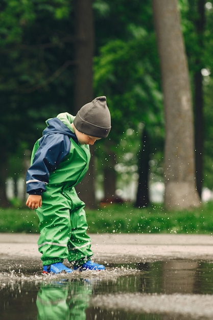 Free photo funny kid in rain boots playing in a rain park