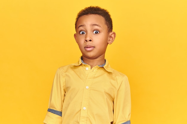 Free photo funny little dark skinned boy expressing total bewilderment, raising eyebrows, staring at camera, being shocked