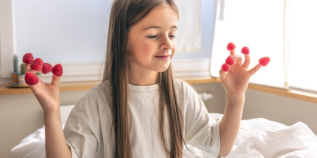 Free photo funny little girl with raspberries on her fingers in bed in the morning