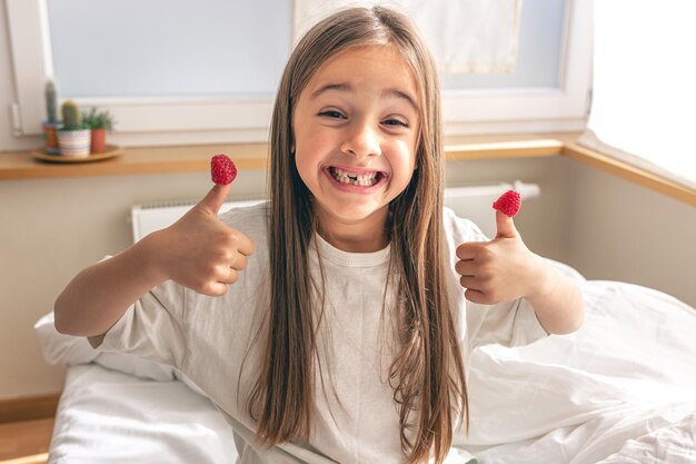 Funny little girl with raspberries on her fingers in bed in the morning