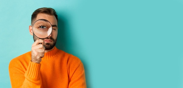 Free Photo funny man looking through magnifying glass searching or investigating something standing in orange s