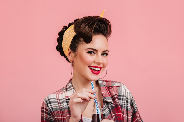 Funny pinup girl smiling on pink background. Studio shot of trendy brunette woman in chckered shirt.