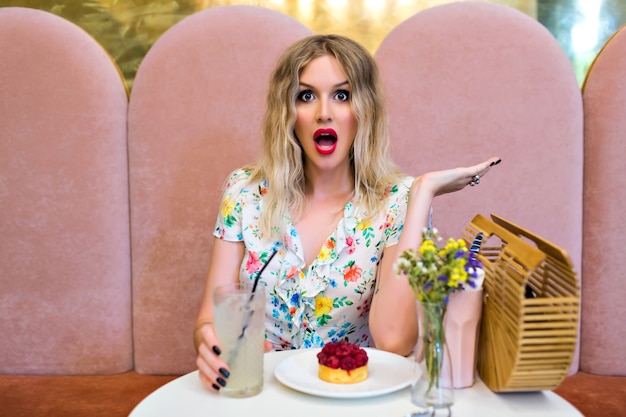 Free Photo funny stylish portrait of blonde woman posing at cute cafe eating dessert, crazy surprised emotions, diet concept, pin up style.