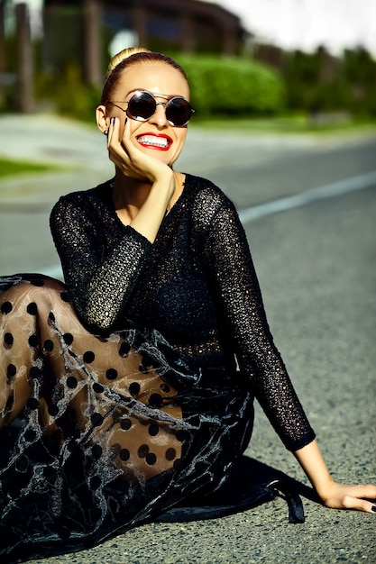 Free photo funny stylish sexy smiling beautiful young blond woman model in summer black  hipster clothes sitting in the street