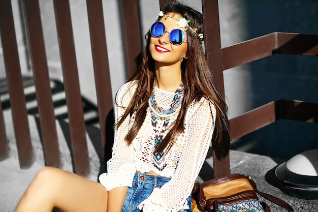 Funny stylish sexy smiling beautiful young hippy woman model in summer white fresh hipster clothes sitting in the street