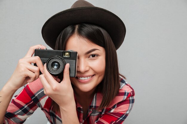 Funny young asian woman isolated over grey wall holding camera.