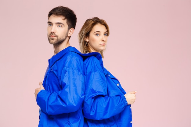 Funny young beautiful couple wearing one jacket  over light pink wall