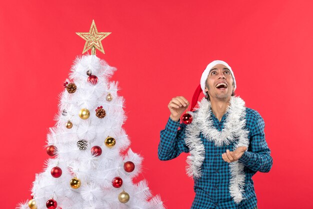 Funny young man with santa claus hat in a blue stripped shirt and holding decoration accessory