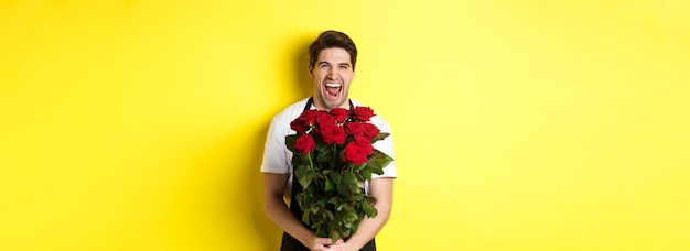 Free photo funny young salesman in black apron holding bouquet of roses florist laughing and standing over yell