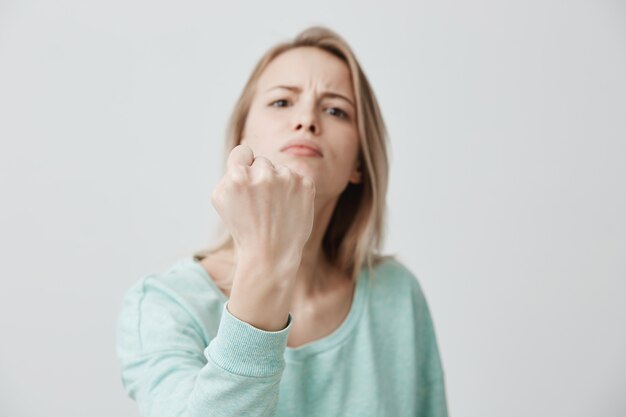 Furious angry displeased young caucasian female frowns face in displeasure, shows clenched fists, demonstrates strength and irritation, annoyed with someone. Negative emotions concept.